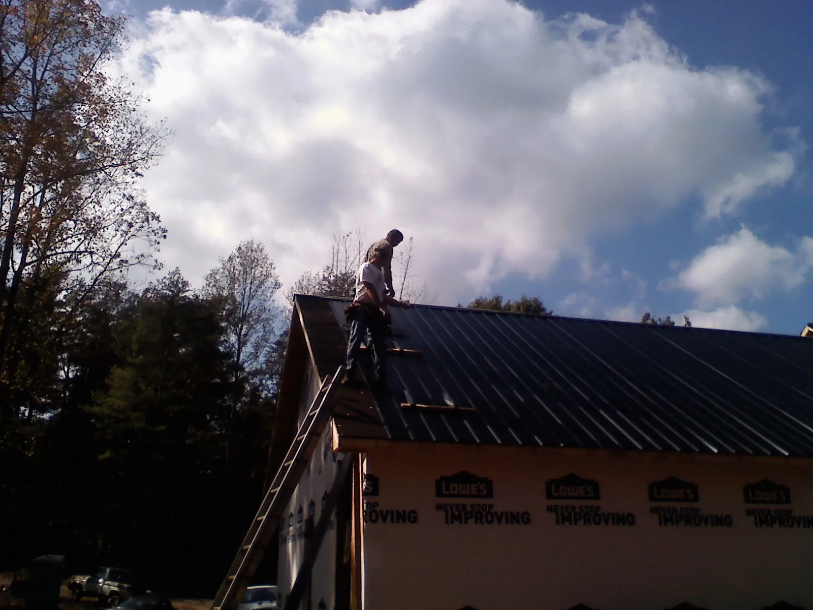 Roofer fastening dark metal panels high against a cloudy sky, from a Roof Inspection job in Medford