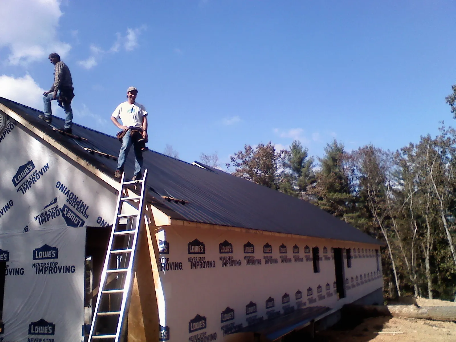 Two roofers standing on a long dark metal roof over a wrapped building in Medford